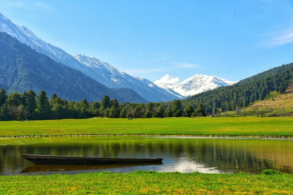 Beautiful summer scene of Pahalgam featuring lush greenery, a tranquil lake, and snowcapped mountains under a clear blue sky.