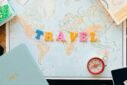 Flat lay of a map with colorful letters "TRAVEL" and a compass for planning adventures.